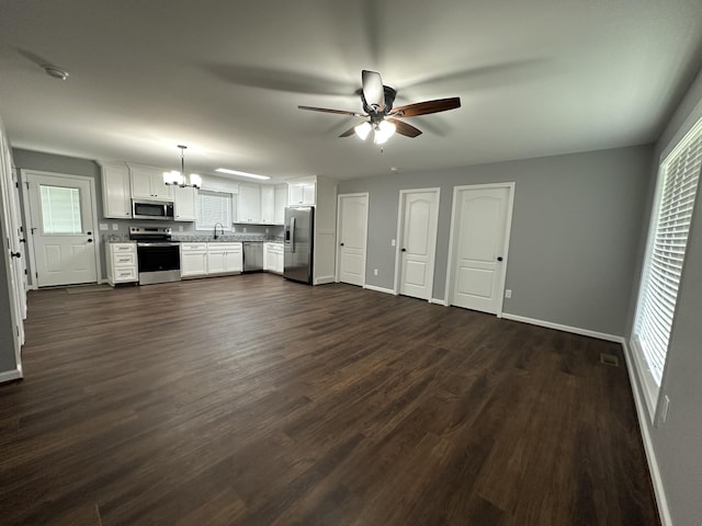 unfurnished living room with dark wood-style floors, a sink, ceiling fan with notable chandelier, and baseboards