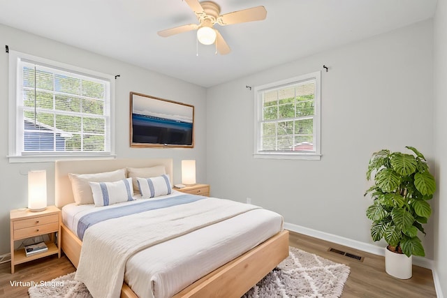 bedroom with baseboards, a ceiling fan, visible vents, and wood finished floors