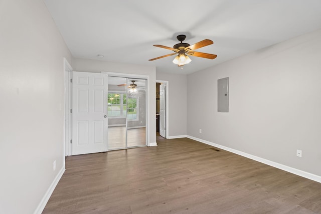 empty room with electric panel, ceiling fan, baseboards, and wood finished floors