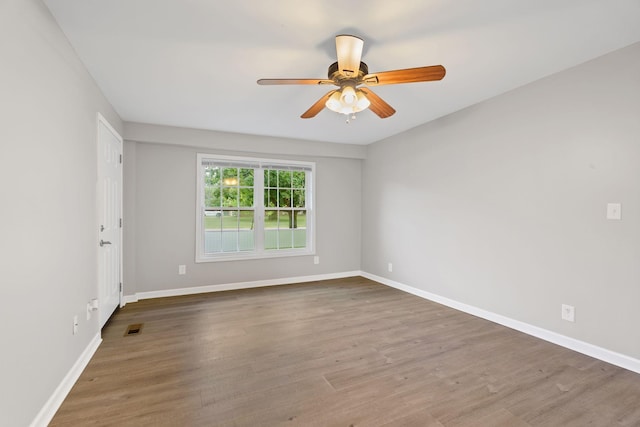 empty room with baseboards, a ceiling fan, visible vents, and wood finished floors