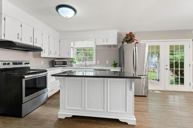 kitchen featuring wood finished floors, a sink, white cabinets, under cabinet range hood, and appliances with stainless steel finishes