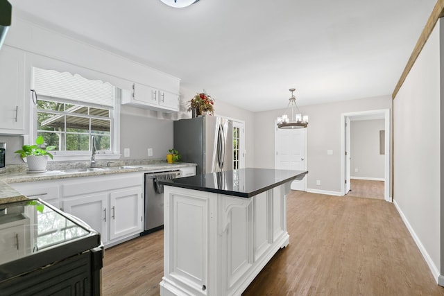 kitchen with a sink, appliances with stainless steel finishes, white cabinets, light wood-style floors, and a kitchen island