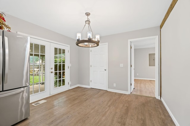unfurnished dining area featuring french doors, baseboards, an inviting chandelier, visible vents, and wood finished floors