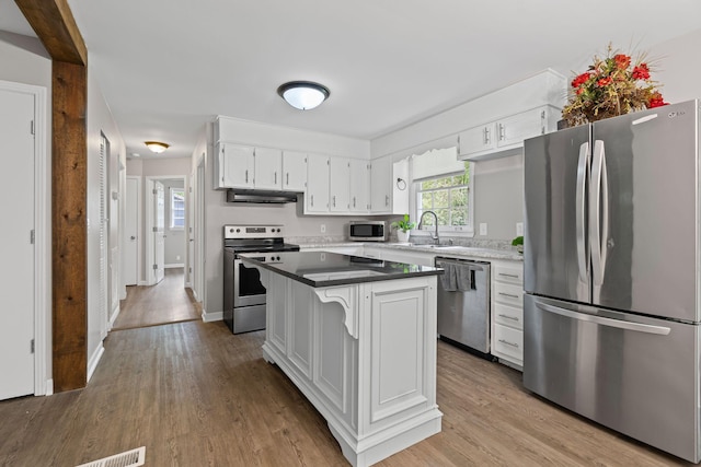 kitchen featuring white cabinets, stainless steel appliances, wood finished floors, and a sink