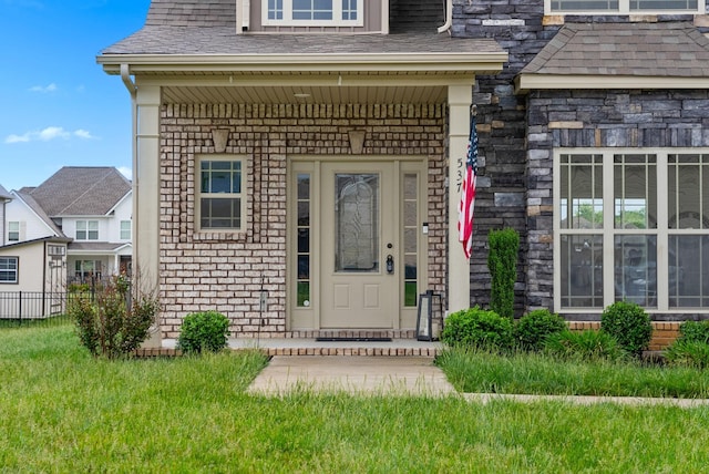 doorway to property featuring a yard, roof with shingles, fence, and brick siding