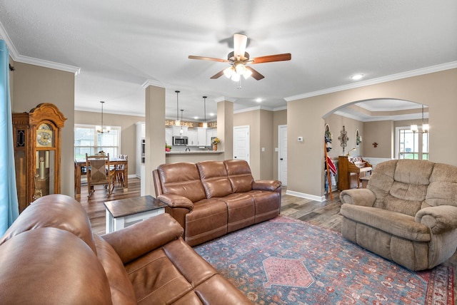 living room featuring ceiling fan with notable chandelier, wood finished floors, crown molding, arched walkways, and baseboards