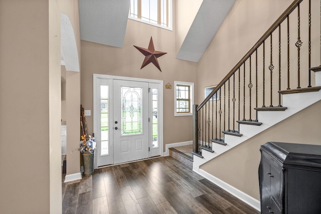 foyer with dark wood-type flooring, baseboards, a towering ceiling, and stairway
