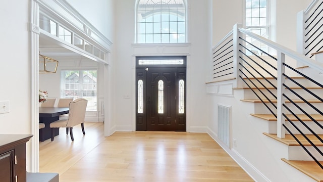 entryway with stairs, a towering ceiling, visible vents, light wood-style flooring, and baseboards
