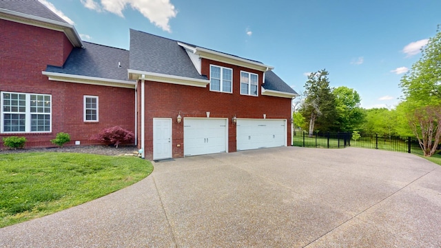 view of side of home with roof with shingles, fence, brick siding, concrete driveway, and a lawn