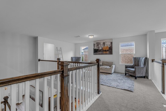 hall with an upstairs landing, healthy amount of natural light, carpet floors, and baseboards