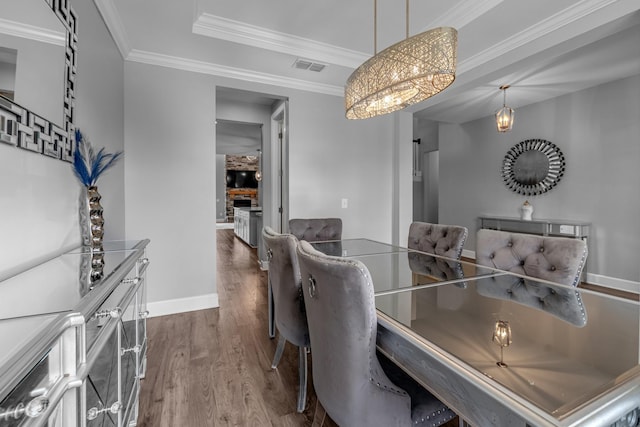 dining room with wood finished floors, baseboards, a chandelier, ornamental molding, and a raised ceiling