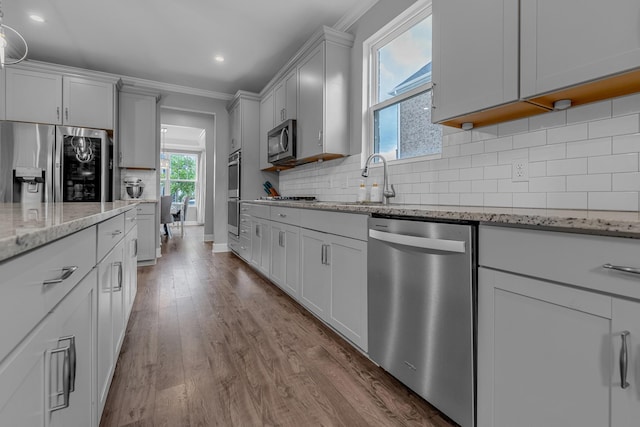 kitchen featuring appliances with stainless steel finishes, ornamental molding, dark wood finished floors, light stone counters, and a sink