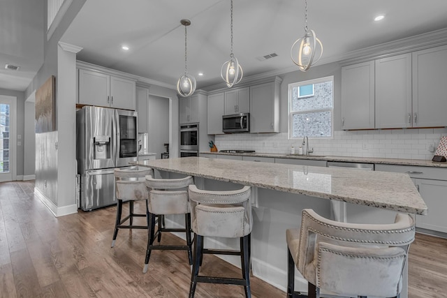 kitchen featuring stainless steel appliances, a sink, gray cabinetry, a kitchen island, and backsplash