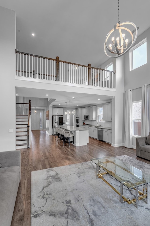 living area with a towering ceiling, a chandelier, stairs, wood finished floors, and baseboards