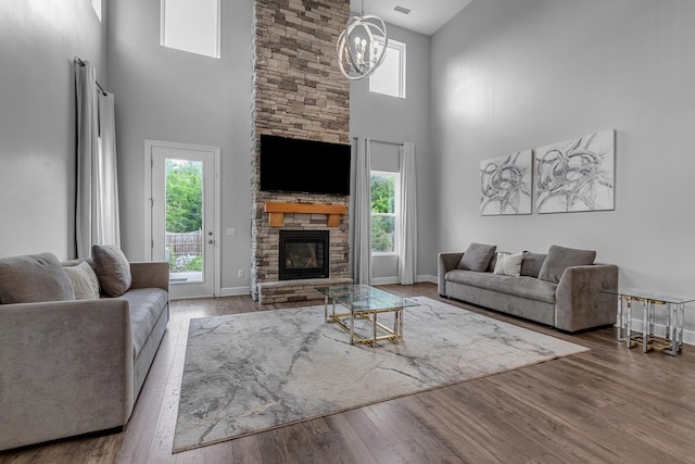 living area with a towering ceiling, a fireplace, baseboards, wood finished floors, and a chandelier