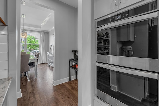 kitchen featuring crown molding, a raised ceiling, dark wood-style flooring, light stone counters, and baseboards