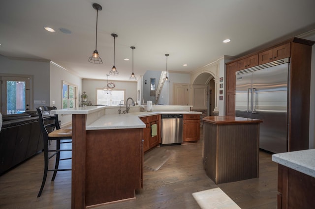 kitchen featuring stainless steel appliances, a large island, arched walkways, a breakfast bar area, and ornamental molding