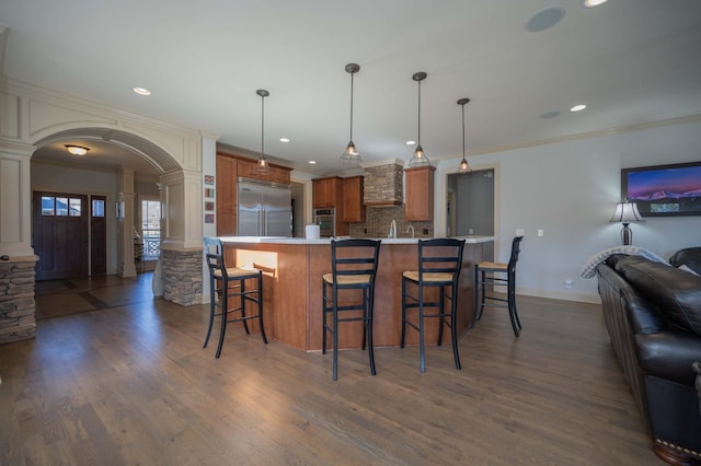 kitchen with appliances with stainless steel finishes, ornate columns, arched walkways, open floor plan, and brown cabinets