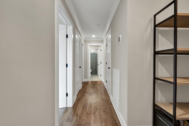 corridor featuring wood-type flooring, ornamental molding, baseboards, and recessed lighting