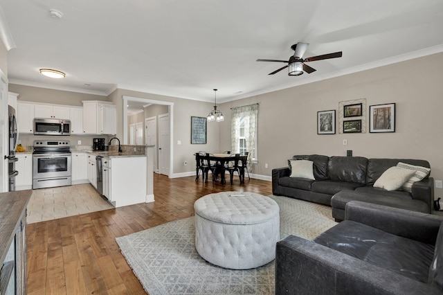 living room featuring hardwood / wood-style flooring, a ceiling fan, ornamental molding, baseboards, and a chandelier