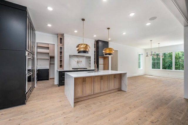 kitchen with light countertops, light wood finished floors, a kitchen island with sink, recessed lighting, and cooktop