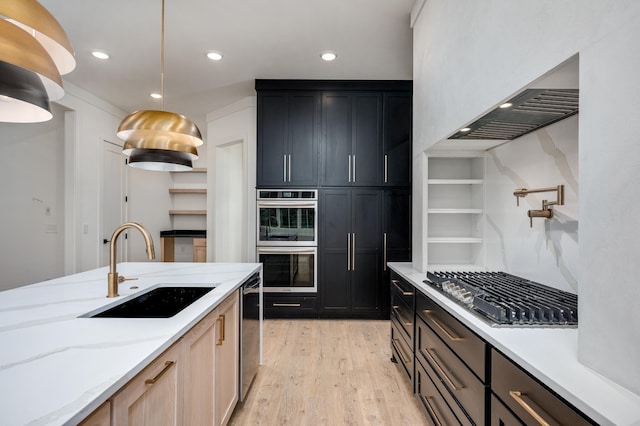 kitchen with a sink, stainless steel appliances, dark cabinetry, light wood finished floors, and light stone counters