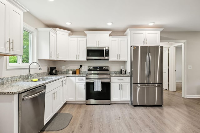 kitchen featuring appliances with stainless steel finishes, a sink, white cabinets, light wood-style floors, and light stone counters