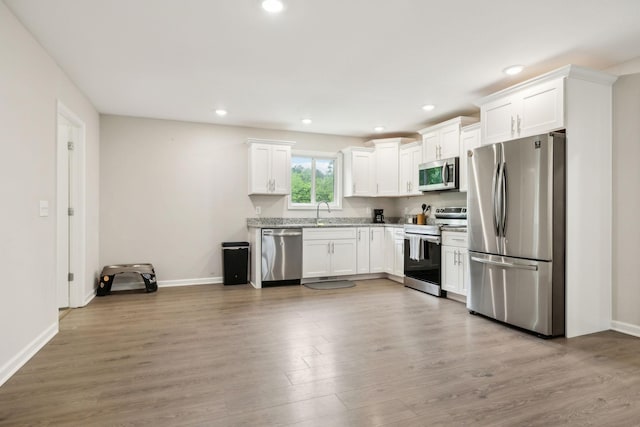 kitchen with appliances with stainless steel finishes, white cabinets, baseboards, and recessed lighting