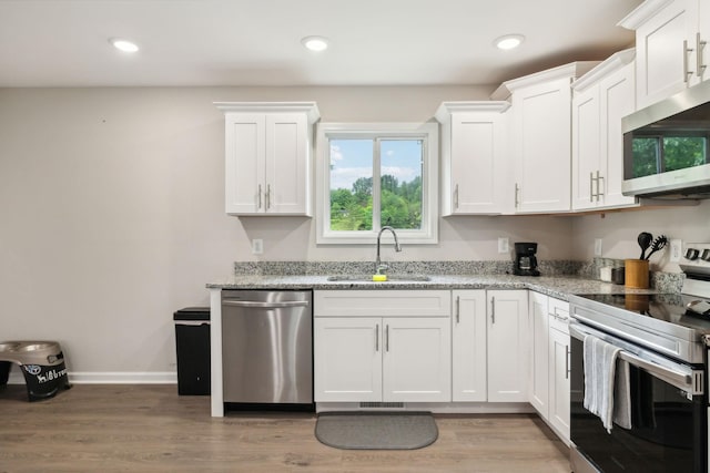 kitchen with appliances with stainless steel finishes, a sink, white cabinetry, light stone counters, and light wood finished floors