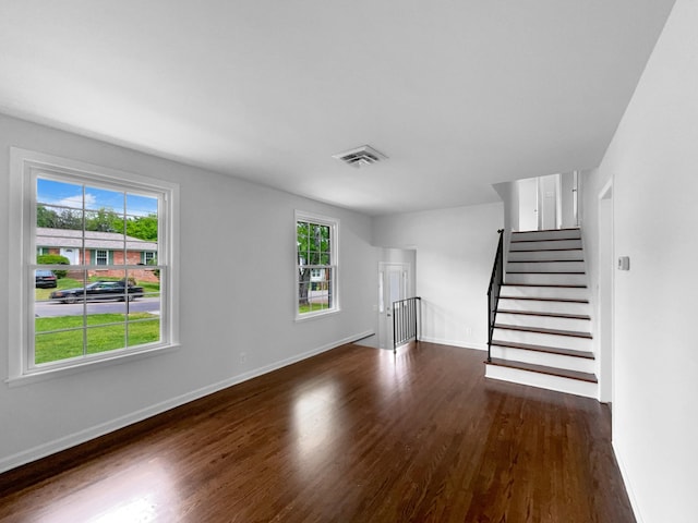 unfurnished living room featuring dark wood-style floors, plenty of natural light, baseboards, and stairs