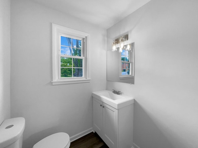half bath with toilet, vanity, baseboards, and wood finished floors