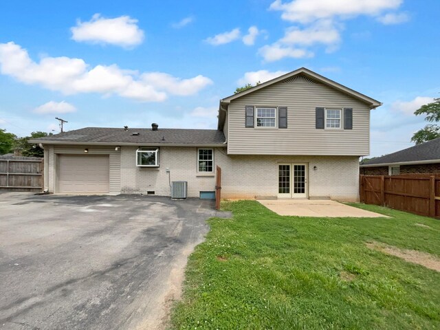 rear view of house featuring an attached garage, brick siding, central AC unit, and asphalt driveway