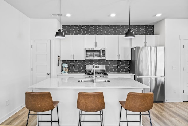 kitchen with stainless steel appliances, a sink, light wood finished floors, baseboards, and white cabinets