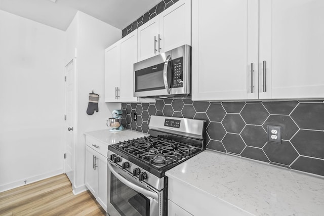 kitchen with appliances with stainless steel finishes, white cabinets, light stone counters, decorative backsplash, and light wood-style floors