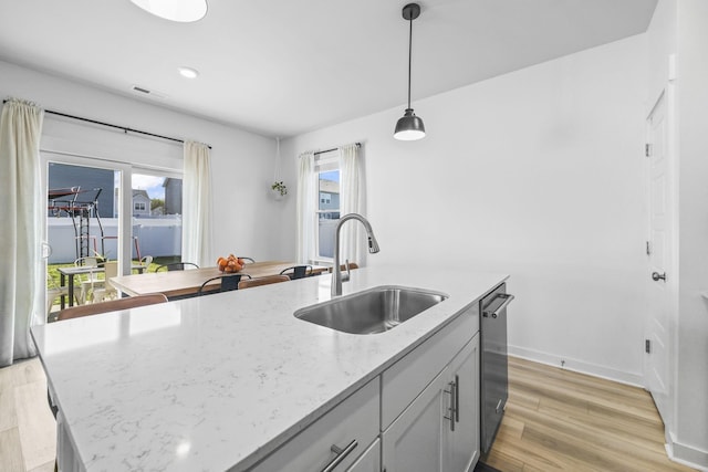 kitchen with a sink, dishwasher, pendant lighting, light wood-style floors, and healthy amount of natural light