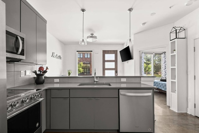 kitchen featuring appliances with stainless steel finishes, gray cabinets, a peninsula, a sink, and concrete flooring