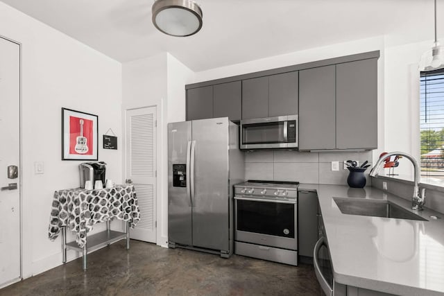 kitchen with appliances with stainless steel finishes, gray cabinets, a sink, finished concrete floors, and tasteful backsplash