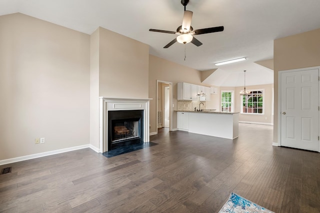 unfurnished living room featuring lofted ceiling, a chandelier, a fireplace with flush hearth, a ceiling fan, and dark wood finished floors