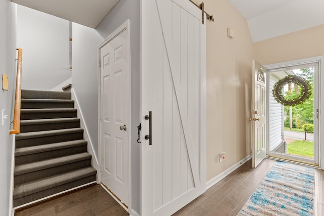 entrance foyer featuring stairs, wood finished floors, a barn door, baseboards, and vaulted ceiling
