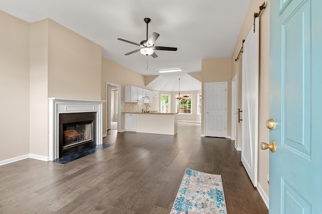 unfurnished living room with a barn door, a sink, ceiling fan, dark wood finished floors, and a fireplace with flush hearth