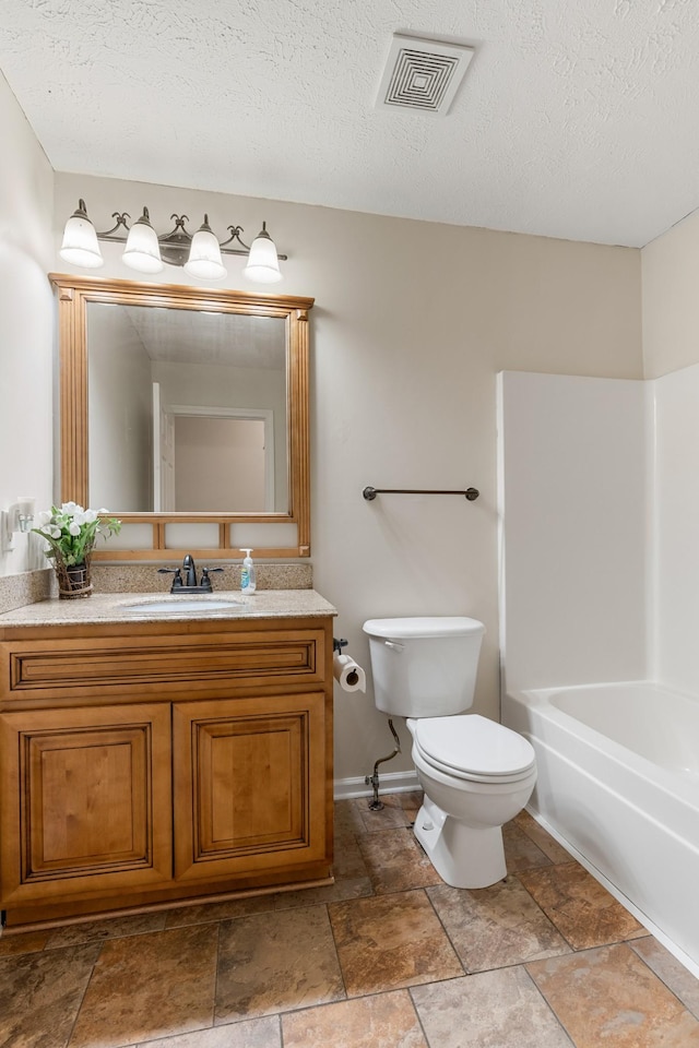 full bath with toilet, vanity, stone finish flooring, and a textured ceiling
