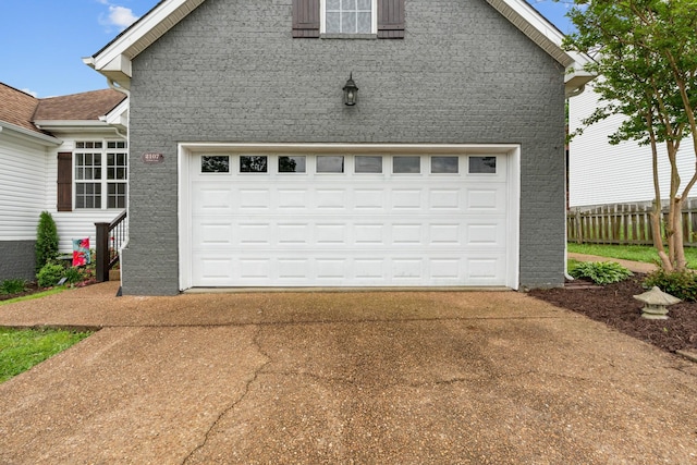 garage featuring concrete driveway and fence