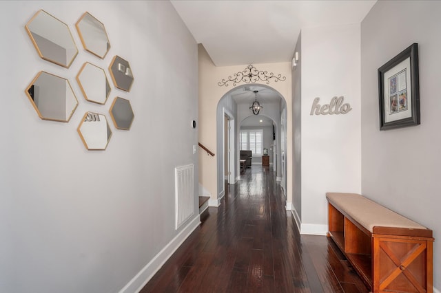 corridor with arched walkways, baseboards, dark wood-type flooring, and stairs