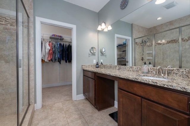 bathroom featuring a shower stall, tile patterned floors, double vanity, a walk in closet, and baseboards