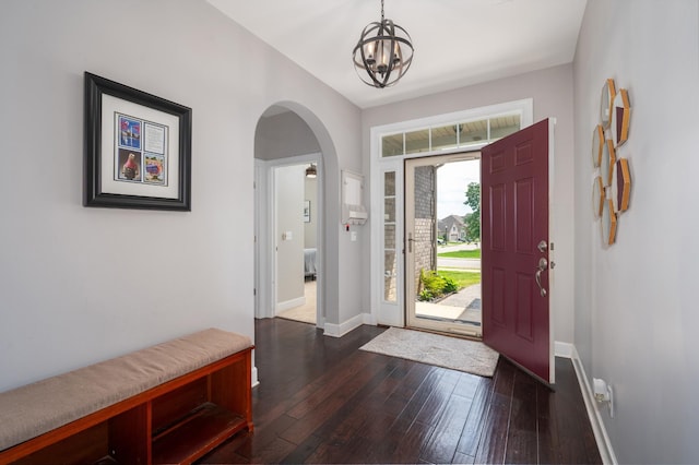 foyer featuring arched walkways, a chandelier, baseboards, and dark wood finished floors