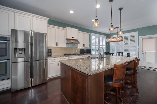 kitchen featuring stainless steel appliances, a sink, a kitchen bar, dark wood-style floors, and recessed lighting