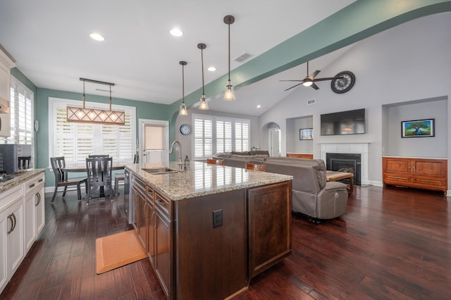 kitchen with arched walkways, a glass covered fireplace, a sink, white cabinetry, and vaulted ceiling