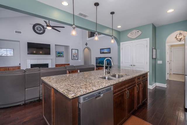 kitchen featuring arched walkways, dishwasher, a sink, a ceiling fan, and a tile fireplace