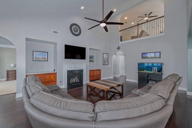 living room with arched walkways, ceiling fan, baseboards, a fireplace with flush hearth, and high vaulted ceiling