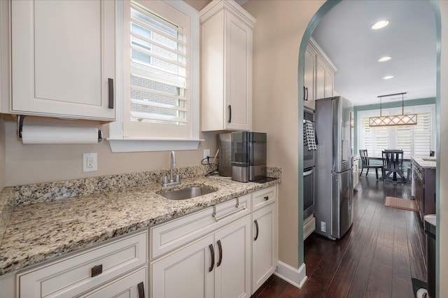 kitchen featuring a sink, freestanding refrigerator, arched walkways, white cabinetry, and light stone counters